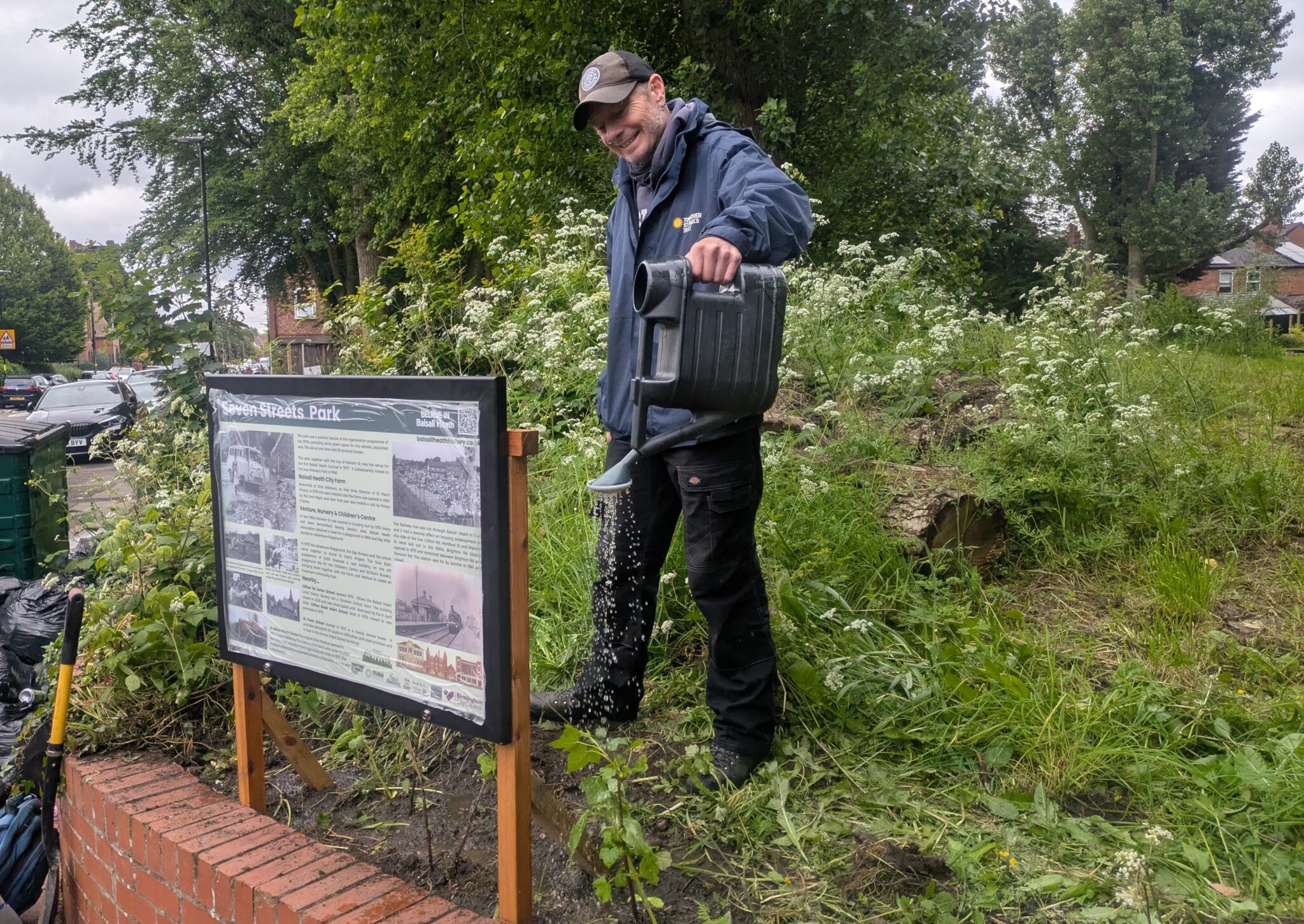 Hywell watering plants by the new history Interpretation Panel